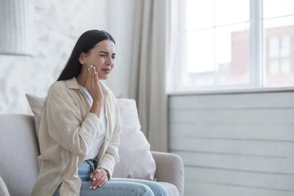 A person sitting on a sofa holding their cheek in pain.