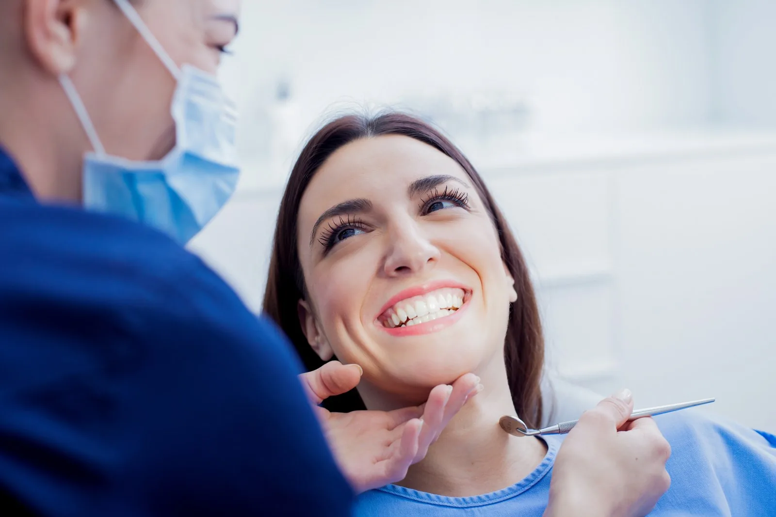 A dentist holding a mouth mirror examines a smiling patient in a dental clinic.